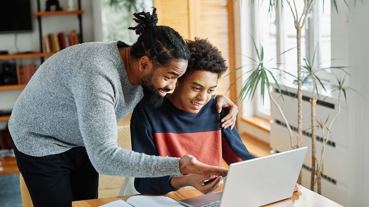 man hugging son pointing to something on laptop in front of son
