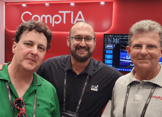 three guys in front of Comp Tia tradeshow booth