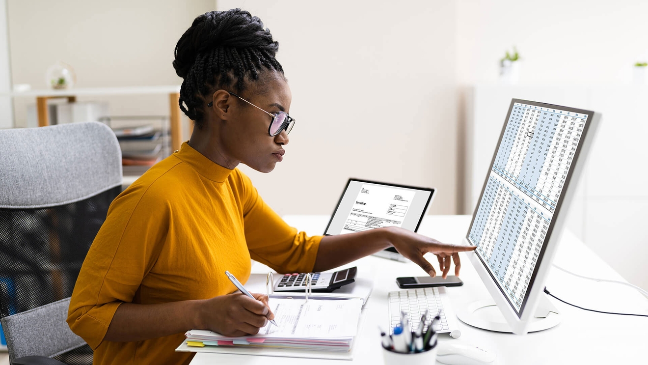 woman pointing at computer while writing something down