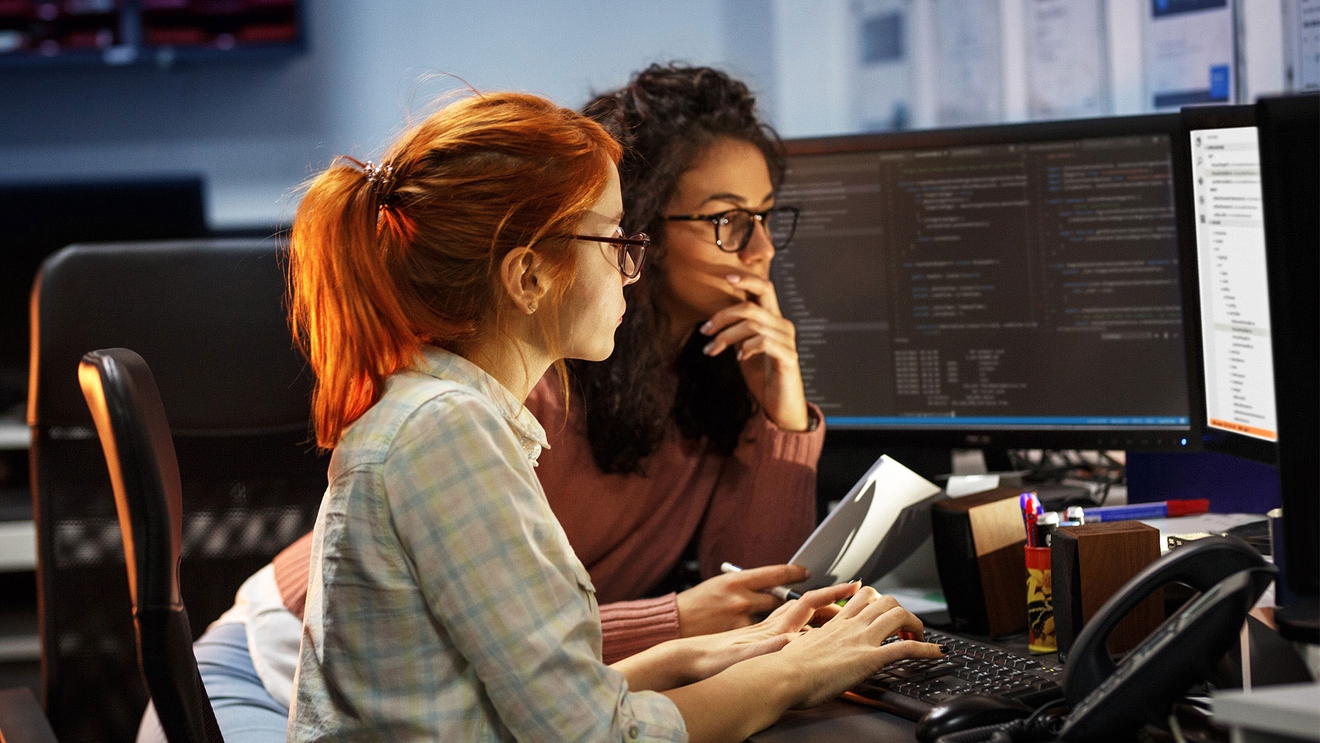 Two people coding on a PC