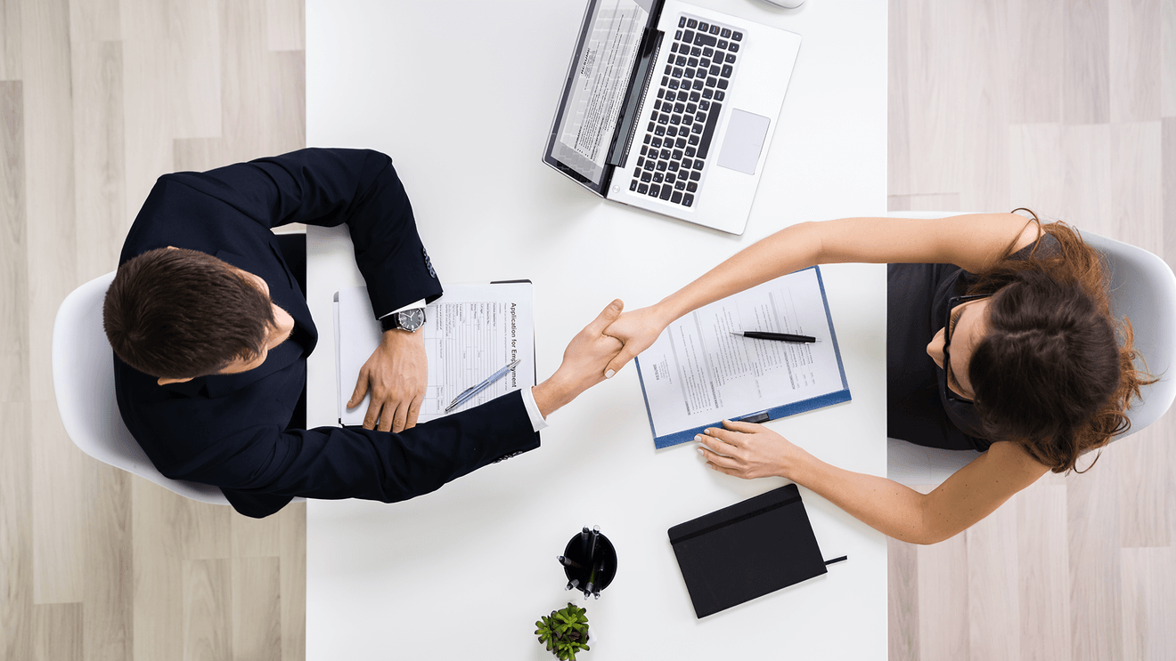 businessman and woman shaking hands with laptop on desk