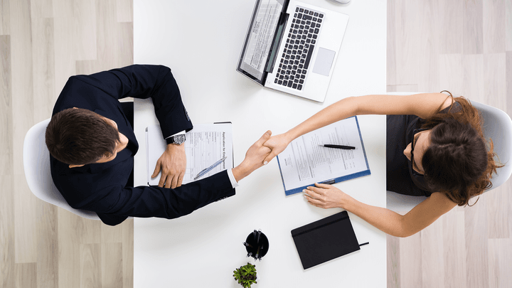 businessman and woman shaking hands with laptop on desk
